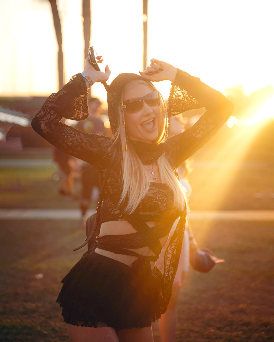 Woman in a black outfit with sunglasses dancing outdoors at sunset.