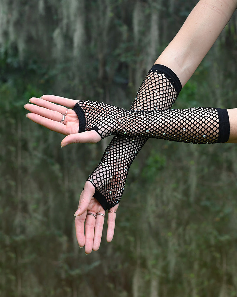 Black fishnet rave gloves worn by a person against a blurred natural background