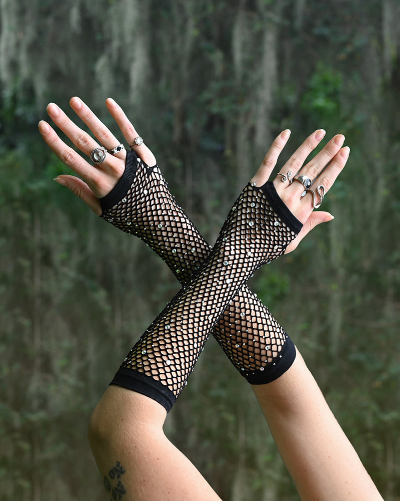 Black fishnet rave gloves worn by a person with a forest background