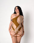 A woman modeling a one-shoulder rave bodysuit with a split design in olive green and beige, accessorized with brown leather garter-style leg straps and chain details, against a plain white studio background.