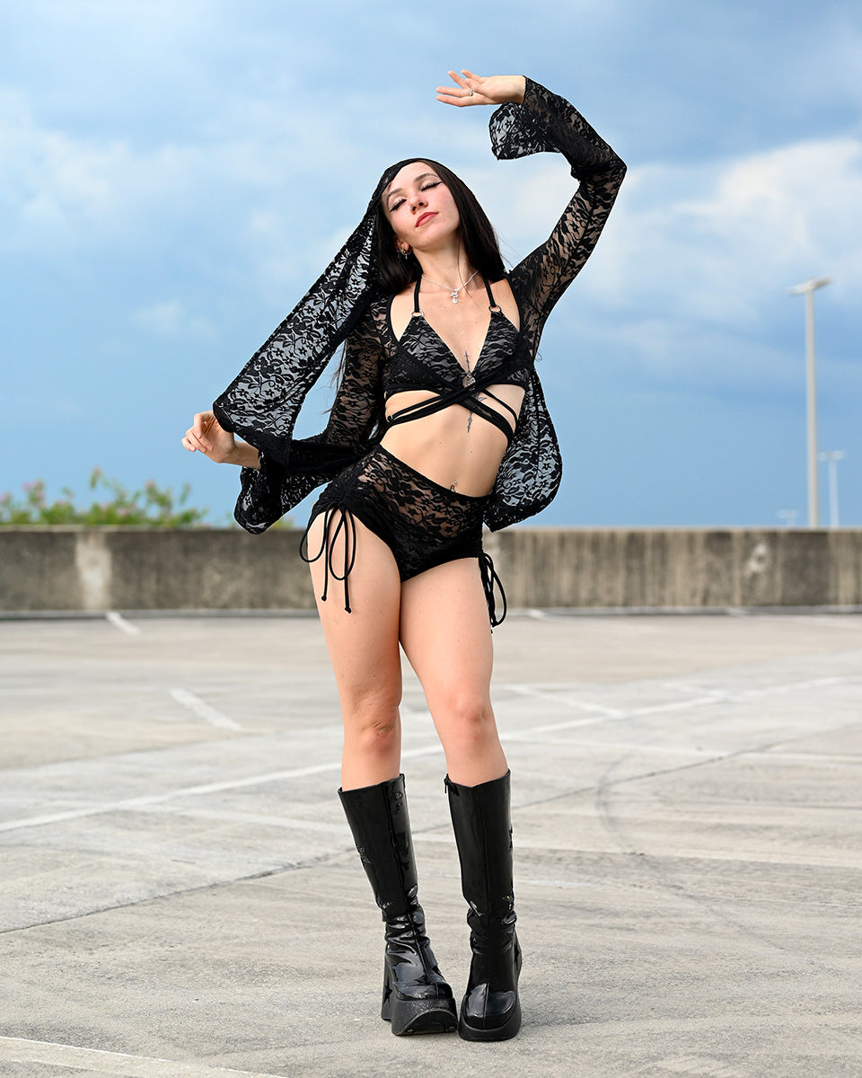 Person wearing a black lace outfit with boots on an outdoor rooftop.