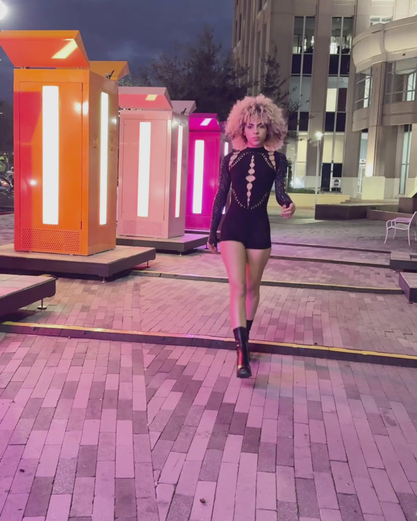 Model wearing a black mesh rave jumpsuit outdoors at night, showing how the jumpsuit looks styled in real world lighting and movement.